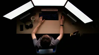 A man sitting in front of three screens